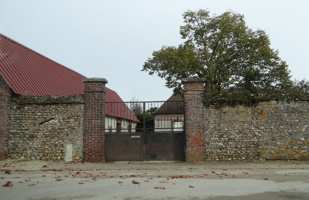 Imposing iron gate surrounded by stone wall, family farm in background