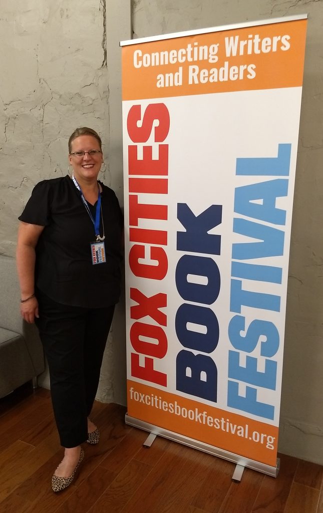Carolyn Porter standing next to a large banner that reads "Fox Cities Book Festival."